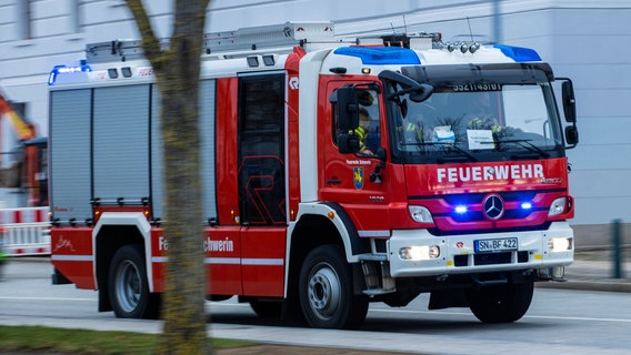 Ein Feuerwehrfahrzeug fährt mit Blaulicht zum Schweriner Schloss. © dpa Foto: Jens Büttner