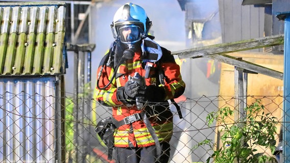 Ein mit Feuerwehrmann in voller Montur läuft auf einen Zaun zu, in den behandschuhten Händen hält er eine Taube. Er trägt eine Gasmaske. © NDR Foto: Tilo Wallrodt