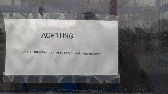 Ein in Klarsichtfolie verpacktes Din A4-Blatt mit der Aufschrift "ACHTUNG Der Flughafen ist vorübergehend geschlossen. © NDR Foto: Christoph Loose