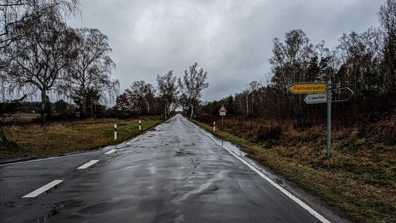 Eine lange, gerade, kleine Straße ohne Spurentrennung und ein Verkehrsschild, das auf den Flughafen Schwerin-Parchim hinweist. © NDR Foto: Christoph Loose