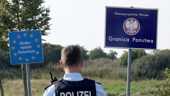 Bei einer flexiblen Schwerpunktkontrolle unmittelbar an der deutsch-polnischen Grenze in der Nähe des ehemaligen Grenzübergang Linken steht ein Bundespolizist vor den Schildern für Deutschland und Polen. © dpa-Bildfunk Foto: Bernd Wüstneck