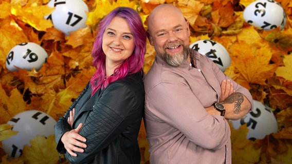 Dania und Stefan stehen im Herbstlaub umgeben von Lottokugeln. © NDR 