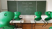 Eine grüne Schultafel auf der mit Kreide geschrieben steht: "Schule entfällt wegen Corona-Virus, Covid-19, SARS-CoV-2". Davor hogestellte Stühle auf Tischen. © imago images / Michael Weber Foto: Michael Weber