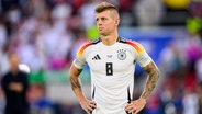 Toni Kroos steht mit den Armen in den Hüften auf dem Spielfeld und schaut enttäuscht. © picture alliance/dpa Foto: Tom Weller