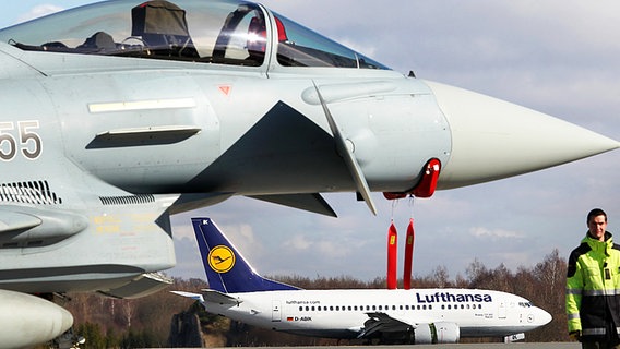 Hinter einem Eurofighter, der in Rostock-Laage stationiert ist, landet die erste Lufthansa-Maschine der neuen Fluglinie von Frankfurt am Main auf dem Rostocker Flughafen. © dpa Foto: Bernd Wüstneck