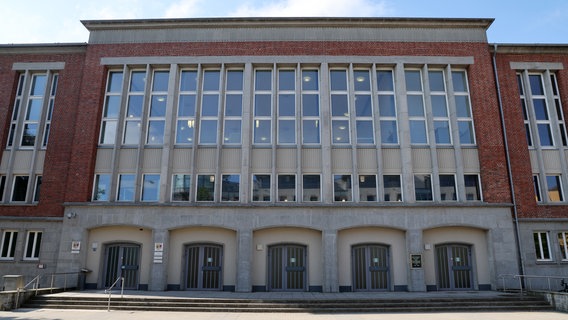 Die Fassade des Rostocker Landgerichts. Über den fünf in steinerne Bogen eingefassten Eingängen prangt eine große Fensterfront. Die Fassade besteht überwiegend aus roten Klinkersteinen. Eine breite Treppe mit drei Stufen führt zu den Eingängen. © picture alliance/dpa Foto: Bernd Wüstneck