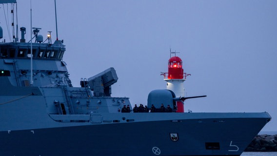 Ein Militärschiff der Bundesmarine fährt am Leuchtfeuer auf der Ostmole von Warnemünde vorbei Richtung Marinestützpunkt Hohe Düne. © picture alliance/dpa Foto: Jens Büttner