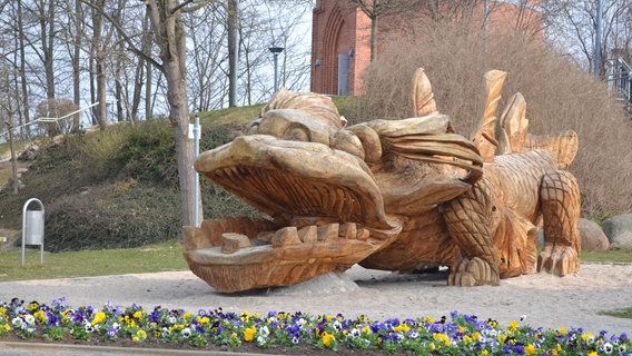 Ein aus Holz geschnitzter Drachen liegt vor dem Wasserturm in Grimmen. © Stadt Grimmen 