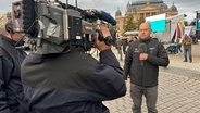 NDR Reporter Christoph Kümmritz steht mit einem Mikrofon vor einem Kamerateam am Alten Garten in Schwerin. © NDR Foto: Jan Baumgart