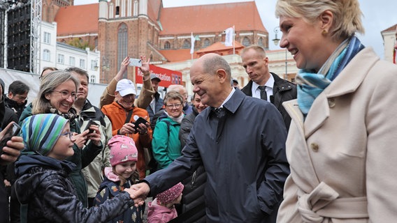 Bundeskanzler Scholz und Bundesratspräsidentin Schwesig unterhalten sich auf dem Weg zum Festakt im Mecklenburgischen Staatstheater mit Bürgern. © dpa Foto: Jens Büttner