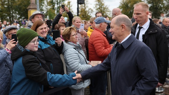 Bundeskanzler Olaf Scholz (SPD) geht nach dem Festakt im Mecklenburgischen Staatstheater durch die Stadt und wird von Bürgern begrüßt. Im Rahmen der Bundesratspräsidentschaft richtet Schwerin unter dem Motto "Vereint Segel setzen" die zentralen Feierlichkeiten zum Tag der Deutschen Einheit aus. © dpa Foto: Jens Büttner