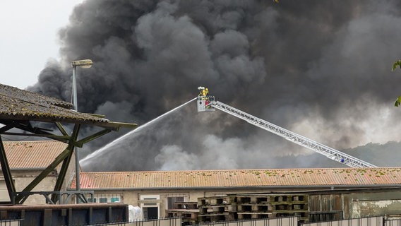 Eine Lagerhalle brennt. Viel Qualm. Ein Feuerwehrmann löscht © NDR Foto: Chris Loose