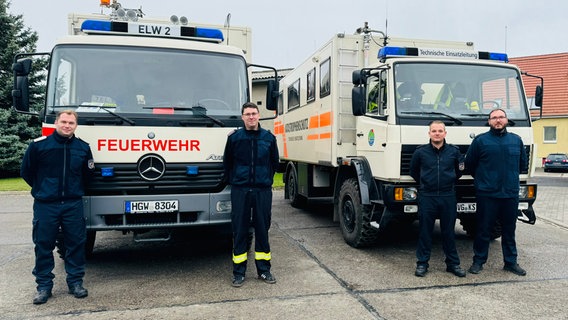 Vier Einsatzkräfte des Katastrophenschutzes stehen vor zwei Einsatzfahrzeugen. © Landkreis Vorpommern-Greifswald 