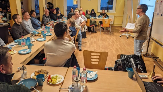 Mehrere Personen sitzen in einem Gemeinschaftsraum an Tischen, auf denen Kaffeebecher und Kuchenteller stehen. © NDR Foto: Katja Bülow