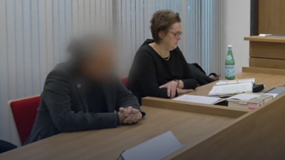 Ein Mann sitzt auf einer Anklagebank. Sein Gesicht ist verpixelt. Daneben sitzt seine Verteidigerin. © NDR 