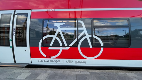 Die rote Außenhaut eines Regionalzugs, auf dem ein großes weißes Fahrradsymbol klebt. © NDR Foto: Christian Kohlhof