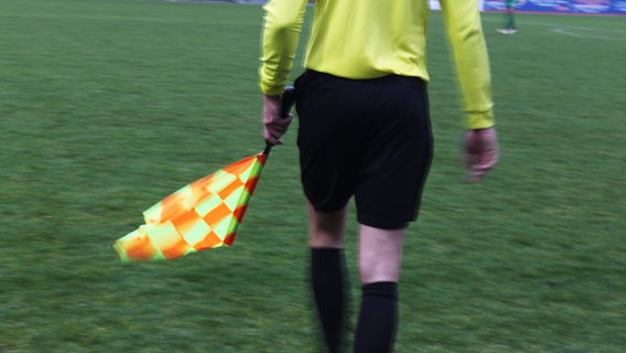 Ein Schiedsrichter geht mit einer Abseitsflagge auf einem Fußballfeld. © NDR Foto: Wiebke Heiden