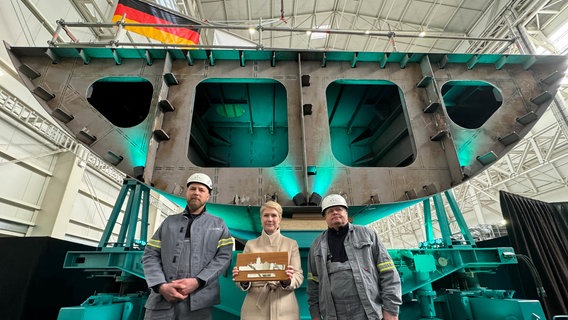 Andre Loth (l-r), Schweißer, Manuela Schwesig (SPD), Mecklenburg-Vorpommerns Ministerpräsidentin, und Heiko Schulz, Schiffbauer, stehen bei der Kiellegung der Flottendienstbootes auf dem Werftgelände der zur Lürssen-Werftengruppe gehörenden Peene-Werft. © dpa-Bildfunk Foto: Stefan Sauer