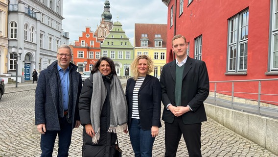 Stefan Fassbinder (Greifswalder Oberbürgermeister), Madeleine Tolani (Präsidentin der Bürgerschaft Greifswald), Anja Rosswinkel (Kanzlei der Bürgerschaft) und Jonas Dietrich (Leiter der Kanzlei der Bürgerschaft) stehen nebeneinander. Im Hintergrund sind die Greifswalder Innenstadt und der Dom zu sehen. © keine Foto: Hannah Freitag