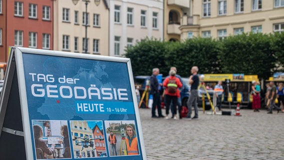 Schild mit der Aufschrift "Tag der Geodäsie" auf dem Markt in Schwerin, im Hintergrund Besucher © NDR Foto: Christoph Loose