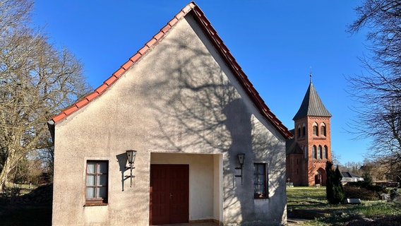 Kleines Gebäude der Trauerhalle auf dem Friedhof in Kritzkow. Im Hintergrund steht die Kirche. © NDR Foto: Juliane Mau