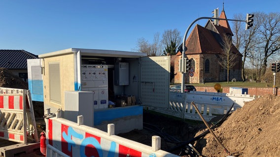 Eine Baustelle mit geöffnetem kleinen Trafohäuschen. Im Hintergrund die Kirche von Satow. © NDR Foto: Danilo Fox