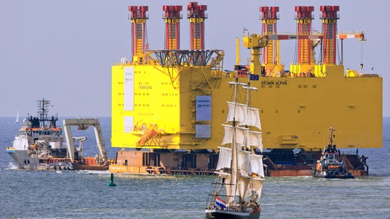 Schlepper zieht die gelbe Offshore-Plattform über das Wasser, begleitet von einem Segelboot. © dpa-Bildfunk Foto: Jens Büttner