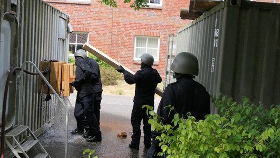 Personen in dunkelblauen Schutzanzügen und mit Militärhelmen bei Übungen zum Löschen und zum Bergen von Verletzten vor einem rot geklinkerten Kasernengebäude. © Bundeswehr, Presse und Informationszentrum des Marinekommandos Foto: Bundeswehr / Herter