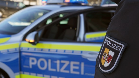 Das Wappen der Polizei Mecklenburg-Vorpommern ist im Vordergrund zu sehen. Im Hintergrund unscharf ein Streifenwagen. © dpa/Marcus Brandt Foto: Marcus Brandt