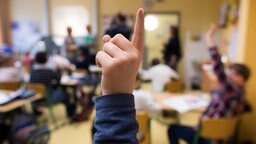 Kind in Schulklasse hebt den Finger.