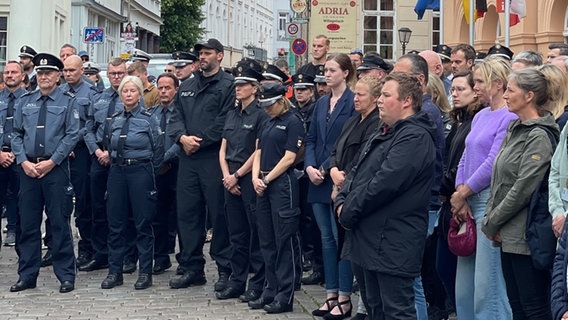 Polizistinnen, Polizisten und Passanten stehen in der Schweriner Innenstadt und gedenken während einer Schweigeminute eines getöteten Polizisten. © Christoph Kümmritz Foto: Christoph Kümmritz