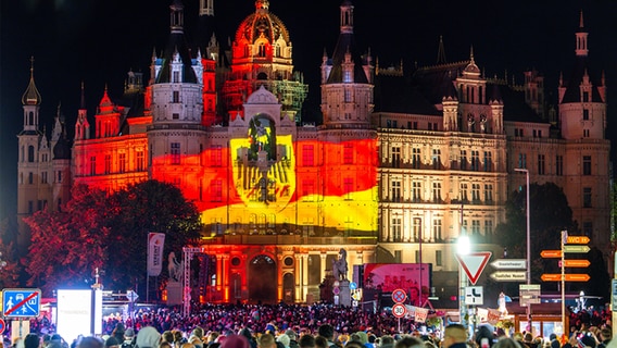 Bei eine Lichtshow, die auf die Fassade des Schweriner Schlosses projiziert wird, können Besucher den Weg von der Friedlichen Revolution 1989 bis heute in Bildern erleben. © dpa Foto: Jens Büttner