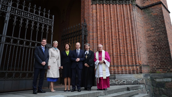 Manuela Schwesig (SPD, 2.v.l), Ministerpräsidentin von Mecklenburg-Vorpommern und derzeitige Bundesratspräsidentin, steht gemeinsam mit ihrem Mann Stefan (l), Bundeskanzler Olaf Scholz (SPD, 3.v.r) und dessen Ehefrau Britta Ernst (3.v.l) vor einem Ökumenischen Gottesdienst mit Landesbischöfin Kristina Kühnbaum-Schmidt (2.v.r) und Erzbischof Heiner Koch vor dem Schweriner Dom. © dpa Foto: Jens Büttner