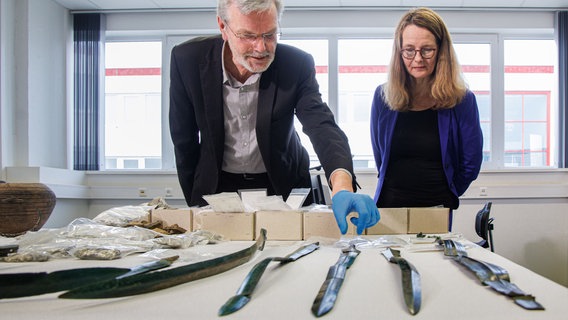 Detlef Jantzen (l), Landesarchäologe von Mecklenburg-Vorpommern, und Bettina Martin (SPD), Ministerin für Wissenschaft und Kultur von Mecklenburg-Vorpommern, betrachten neueste archäologische Funde aus Mecklenburg-Vorpommern - darunter einen Silberschatz aus dem 11. Jahrhundert mit rund 6000 Münzen sowie sieben zum Teil kostbar verzierte Bronze-Schwerter aus vorchristlicher Zeit. © dpa Foto: Markus Scholz