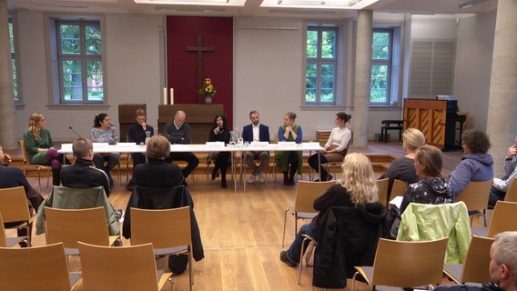 Teilnehmer einer Podiumsdiskussion sprechen im Podium und mehrere Gäste hören zu. © Screenshot 