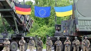 Deutsche und ukrainische Soldaten stehen beim Besuch des ukrainischen Präsidenten Selenskyj auf einem Truppenübungsplatz vor Flugabwehrraketensystemen vom Typ Patriot. © dpa-Bildfunk Foto: Jens Büttner