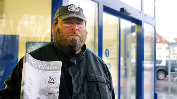 Verkäufer Torsten steht mit einem Exemplar der Straßenzeitung "Der Strohhalm" in Rostock vor einem Einkaufszentrum. © Frank Schlößer Foto: Frank Schlößer