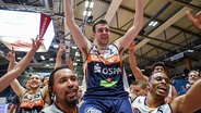 Der Basketballspieler Tyler Nelson wirft jubelnd die Hände in die Höhe, während er von seinen Teamkameraden bei den Rostock Seawolves auf den Schultern getragen wird. Sein Treffer sicherte dem Team den Aufstieg in die Basketball Bundesliga. © Rostock Seawolves Foto: Stefan Junghanns