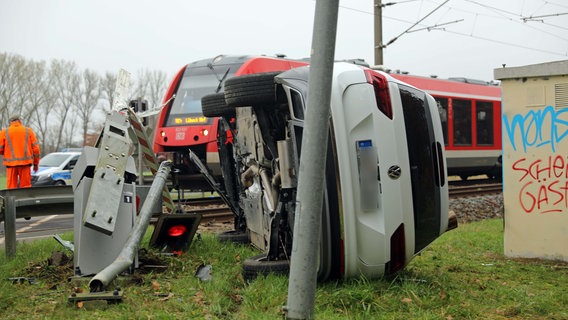 Ein Auto liegt auf der Seite neben einer zerstörten Schranke an einem Bahnübergang. Im Hintergrund steht ein Zug auf den Gleisen. © Stefan Tretropp Foto: Stefan Tretropp