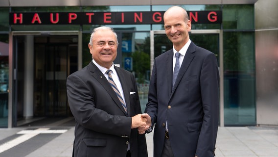 Prof. Krause und Prof. Reisinger reichen sich die Hände vor einem Gebäude der Universitätsmedizin Rostock. © Universitätsmedizin Rostock Foto: Stefan Menzel