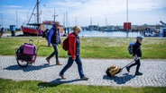 Die ersten auswärtigen Urlauber ziehen nach der Auflösung der Reisesperre wegen der Corona-Schutzmaßnahmen ihre Koffer im Hafen von Kloster auf der Insel Hiddensee zu ihren Urlaubsunterkünften. © dpa-Bildfunk Foto: Jens Büttner