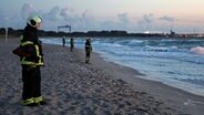 Rettungskräfte stehen in der Abenddämmerung am Strand und suchen die Ostsee nach einem Vermissten ab. © NDR Foto: Stefan Tretropp