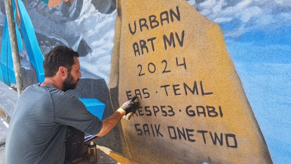 Ein Graffitikünstler sprüht ein Bild an eine Wand. © NDR Foto: Dörto Rochow