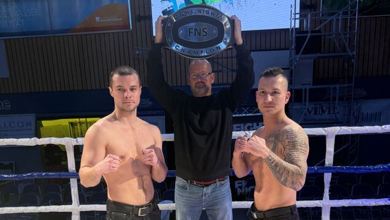 Die Boxer Oleksandr Chernomorets und Sebastian Möller posieren im Ring. Im Hintergrund hält ein Trainer einen Box-Gürtel hoch. © Allround Sport Gym Foto: Christian Bürki