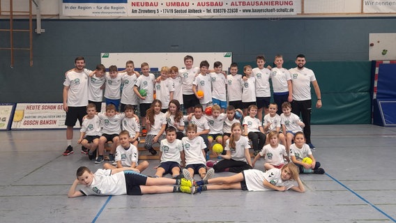 Handball-Jugendspieler und zwei Trainer präsentieren sich in einer Sporthalle. © HSV Insel Usedom 