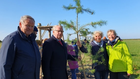 Bürgermeister Holger Kliewe, Landwirtschaftsminister Till Backhaus sowie Silke Stephan und Katharina Dujesiefken vom BUND M-V stehen neben einer jungen Kiefer. © Susann Schmorell 