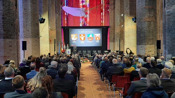 Viele Menschen sitzen in der wiederaufgebauten Nikolaikirche. Vor einer Leinwand moderieren Bürgermeister Galander und Bürgervorsteher Brüsch. © NDR Foto: M. Klemme