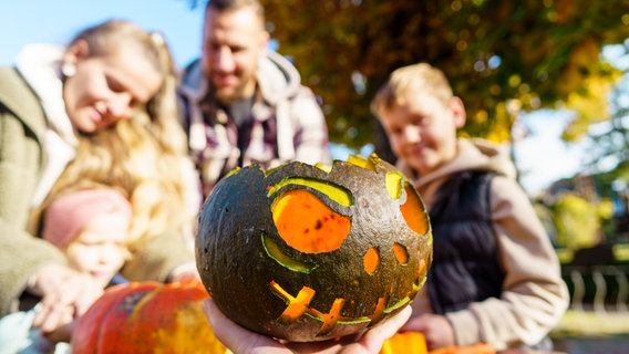 eine dunkel angemalte Halloween-Kürbismaske im Vordergrund, dahinter etwas unscharf Familien mit Kindern © Kur - und Tourismus GmbH Zingst, Pressestelle 