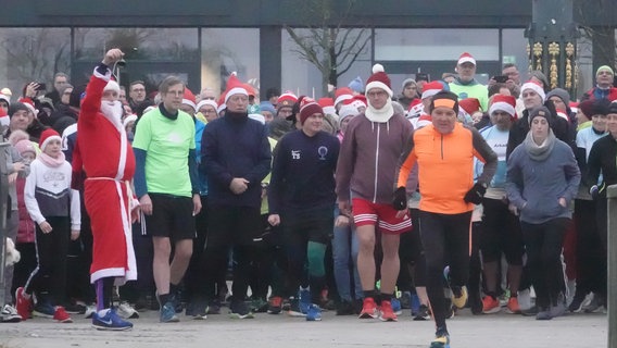 Eine Gruppe von Läufern steht an der Startlinie und den Startschuss gibt ein Mann in einem Weihnachtsmannkostüm. © Matthias Gründling Foto: Matthias Gründling