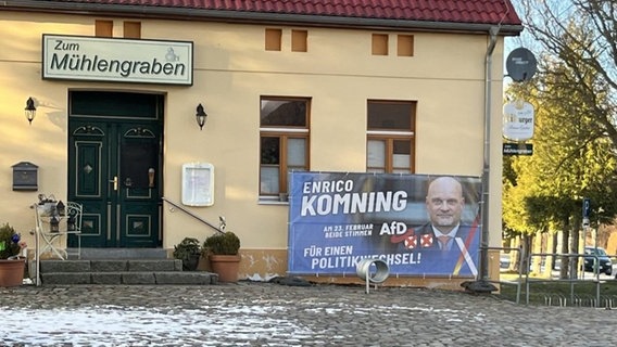 Neben dem Eingang einer Kneipe und einem Gemeindehaus steht ein großes Wahlplakat der AfD. © NDR Foto: G. Hoffmann